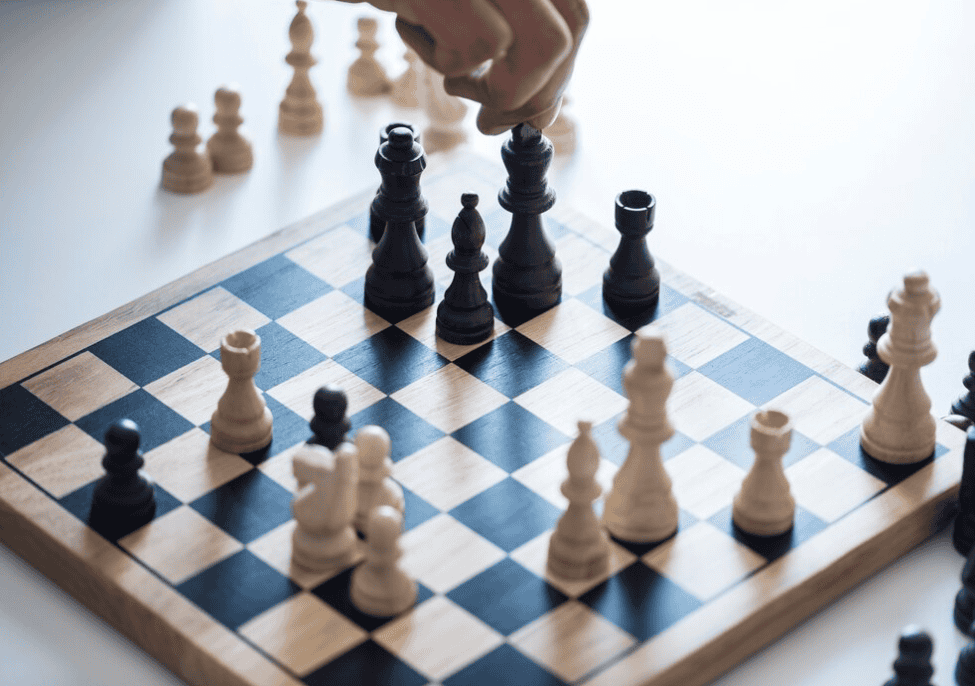 Hand moving a black chess piece amidst white and black pieces