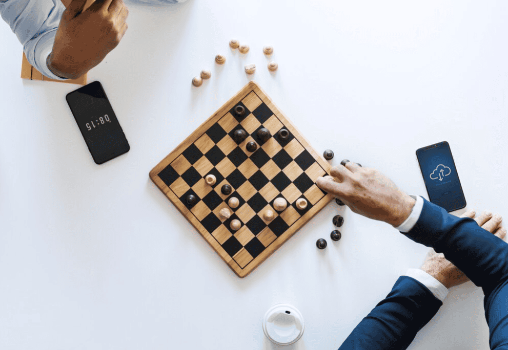 two players with a draughts board between them, smartphones beside