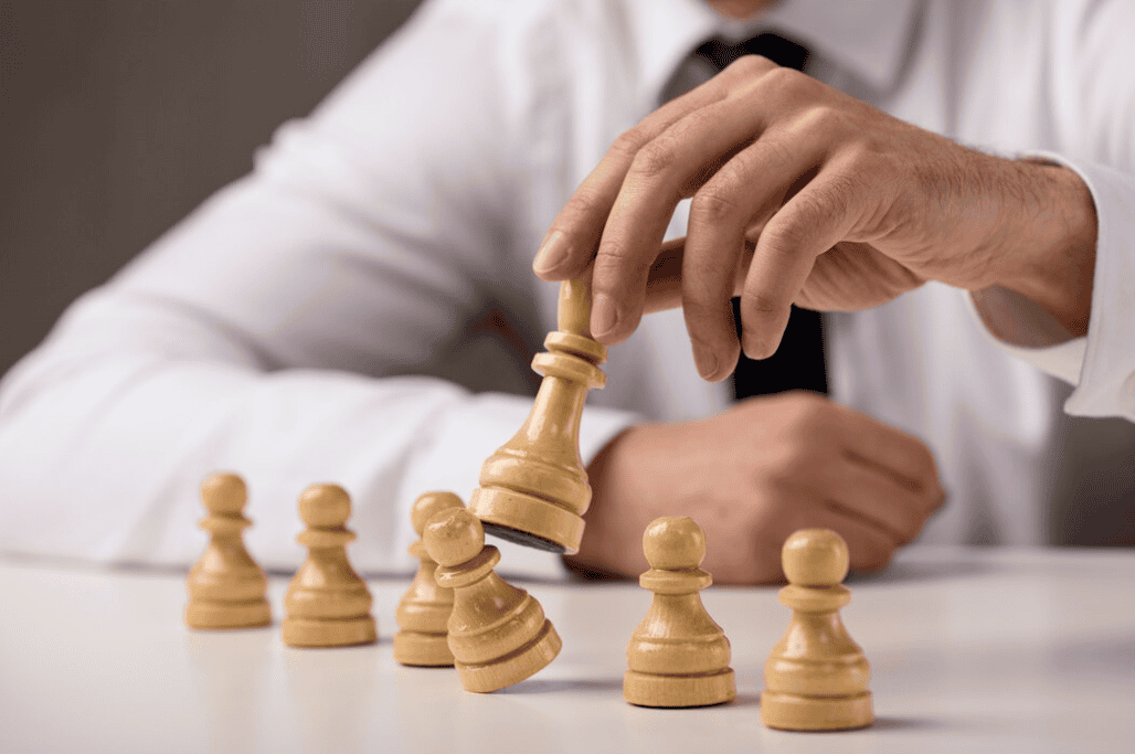 A person in formal attire moving a wooden chess king among other chess pieces