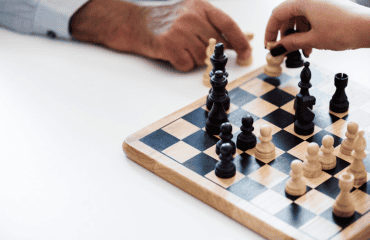 Two hands, one from each player, making moves on a wooden chessboard with black and white pieces
