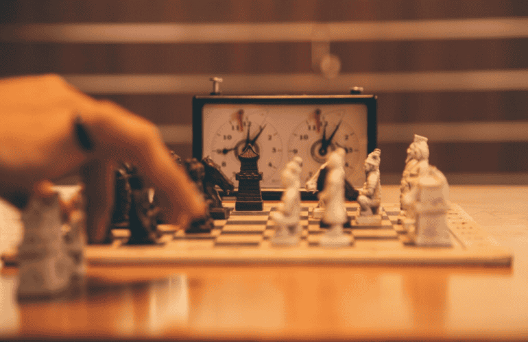 A hand near a chessboard with a chess clock in the background