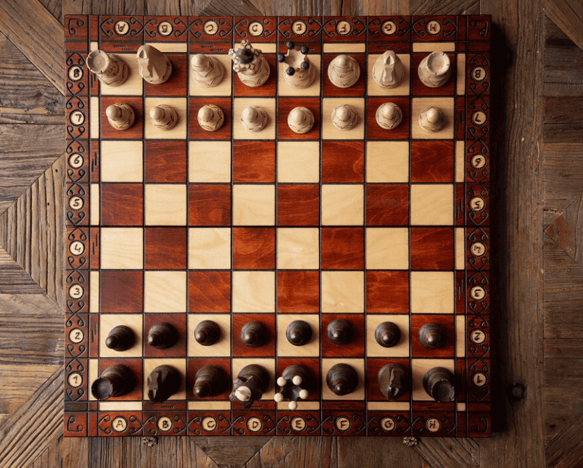 wooden chessboard with light and dark squares, ornate border detailing, and set chess pieces